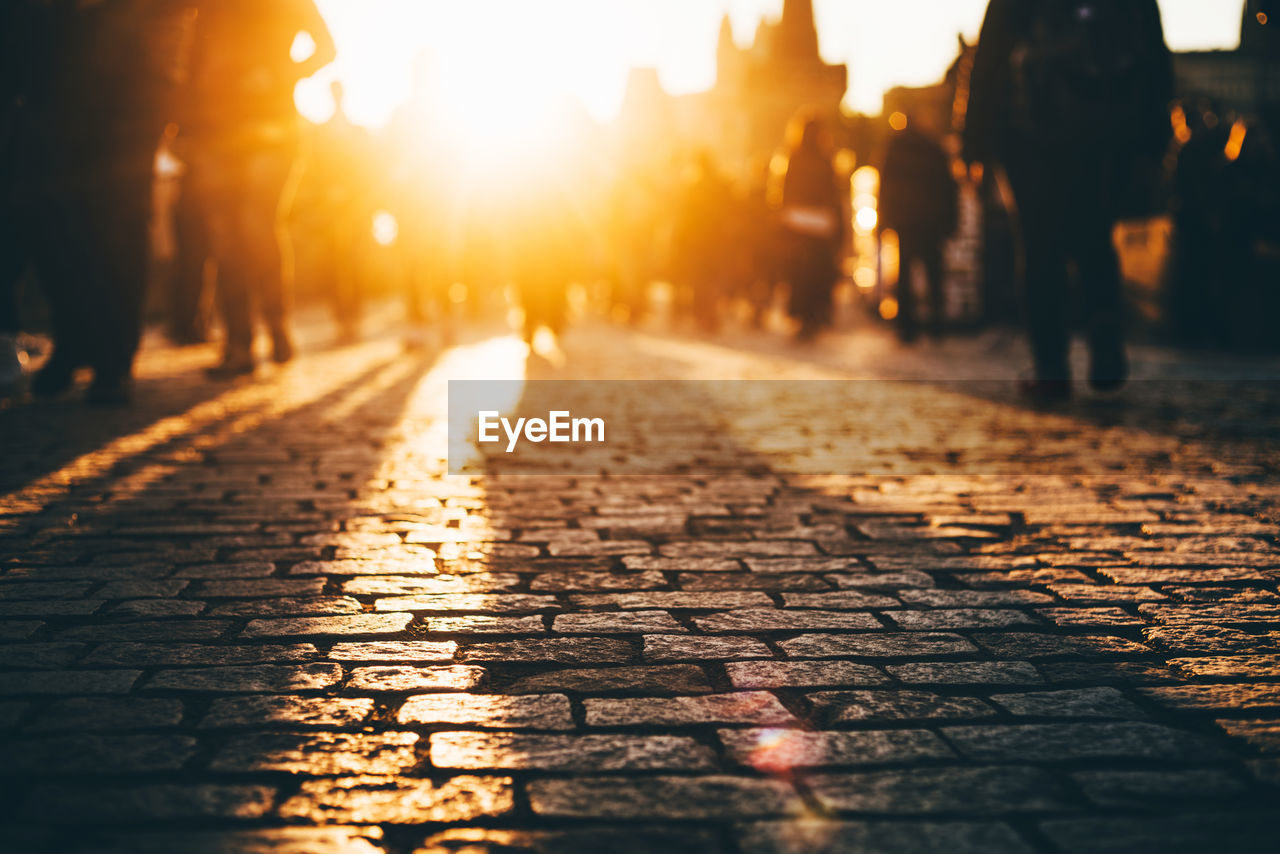 Surface level of people walking on footpath in city at sunset