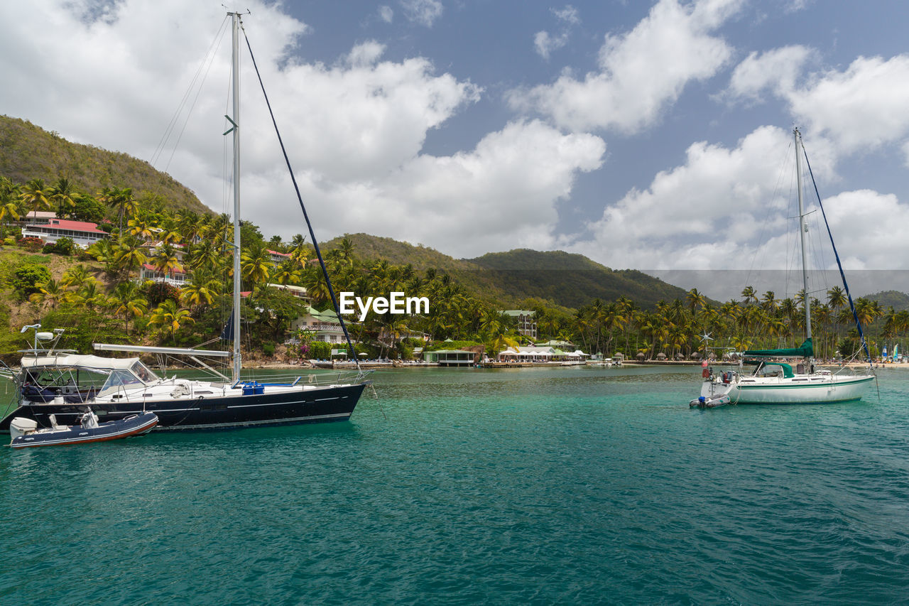 SAILBOATS MOORED ON SEA BY MOUNTAINS AGAINST SKY