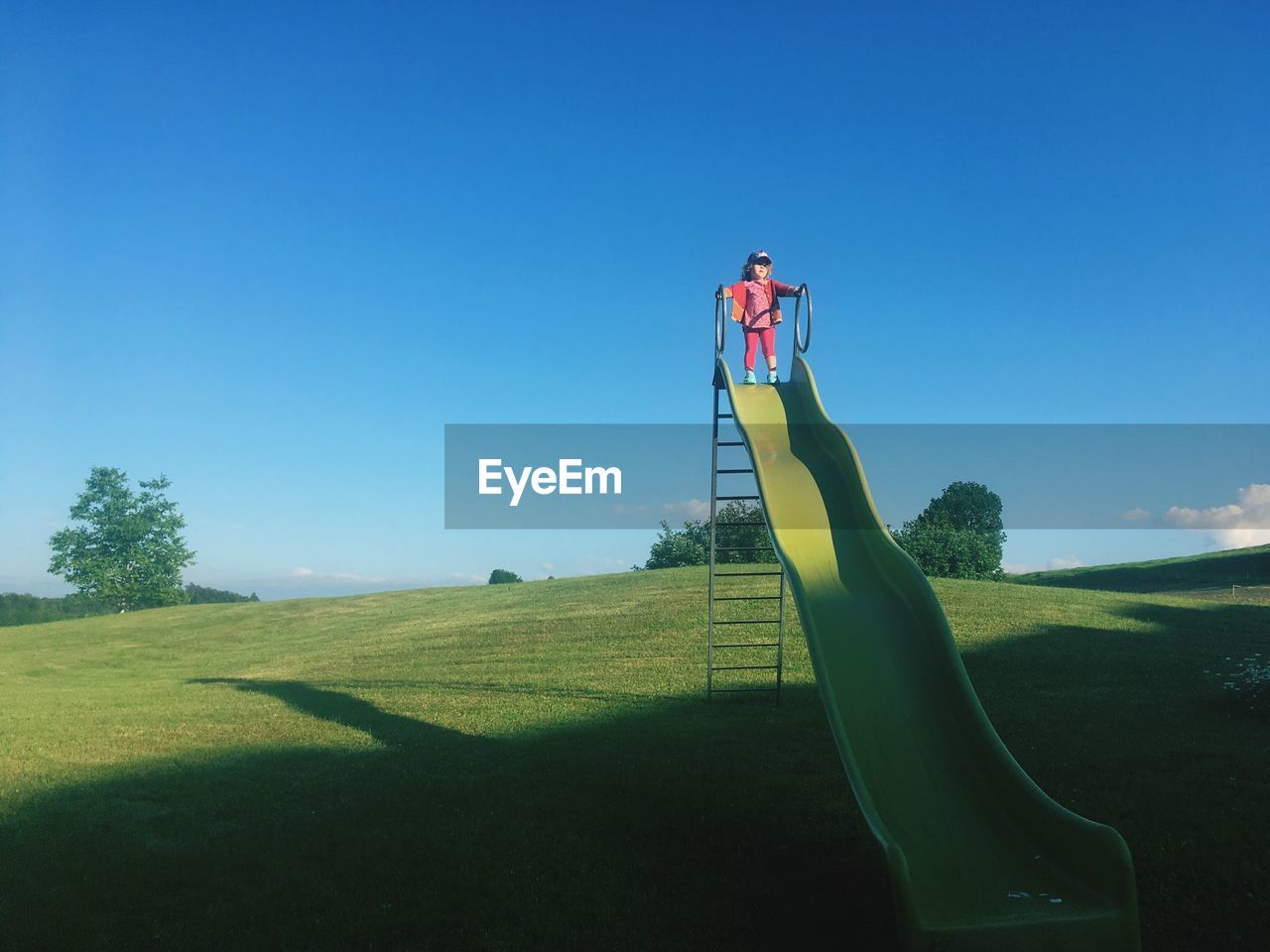 Full length of girl standing on slide at field against sky