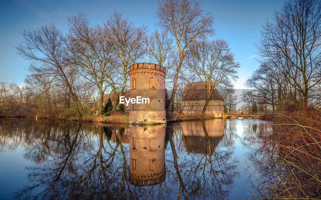 Reflection of bare trees in moat of a castle against sky
