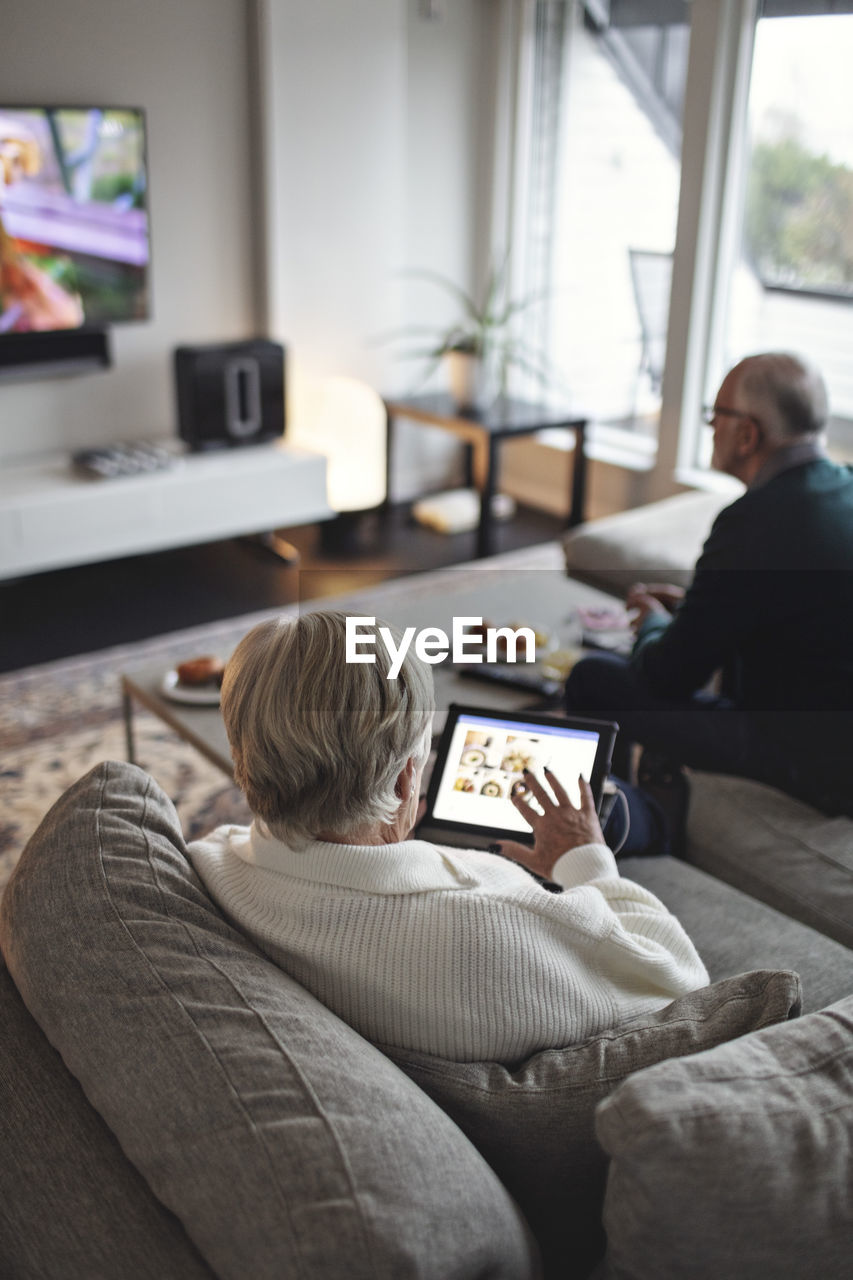 High angle view of senior woman using digital tablet while male partner sitting on sofa in living room