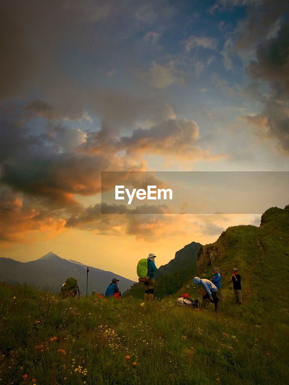 PEOPLE ON FIELD BY MOUNTAINS AGAINST SKY DURING SUNSET