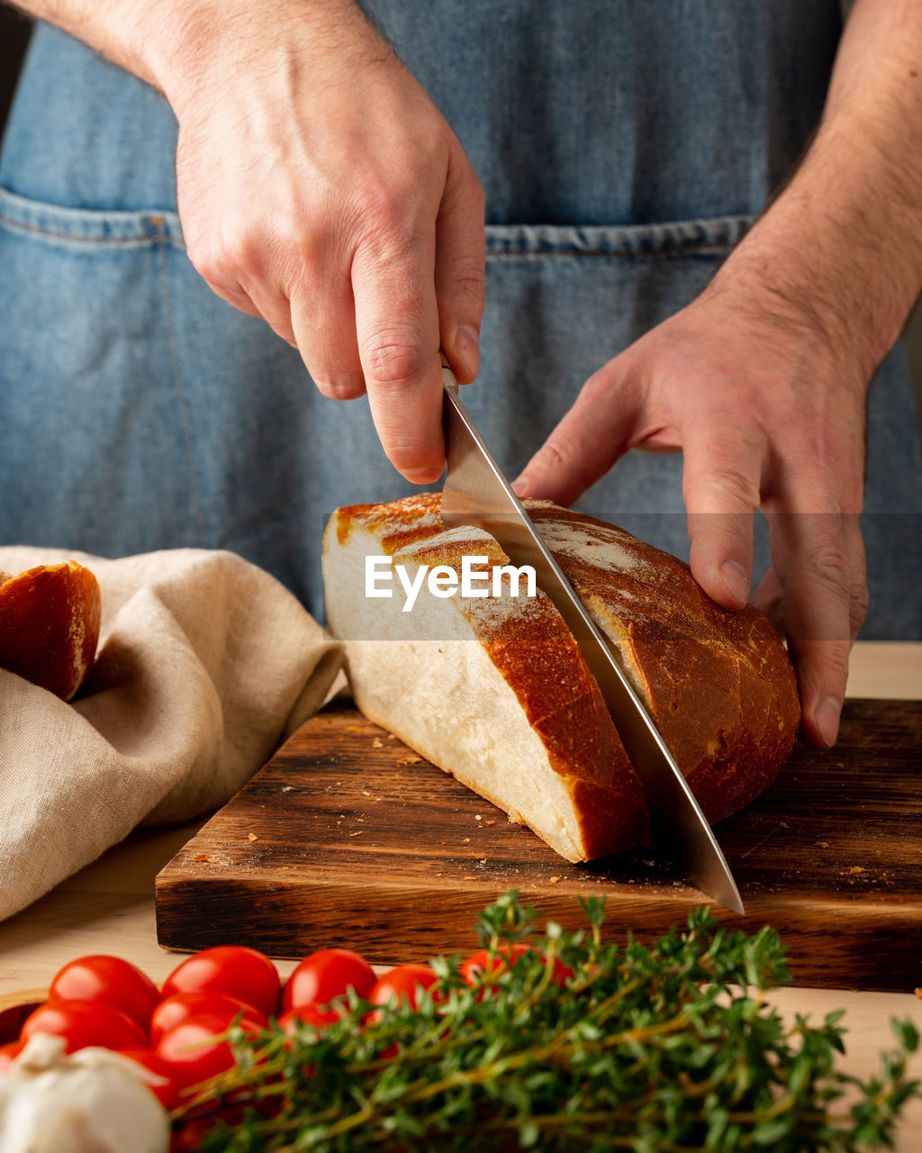 Faceless man cutting fresh home baked crusty bread with large knife on wooden board on kitchen 