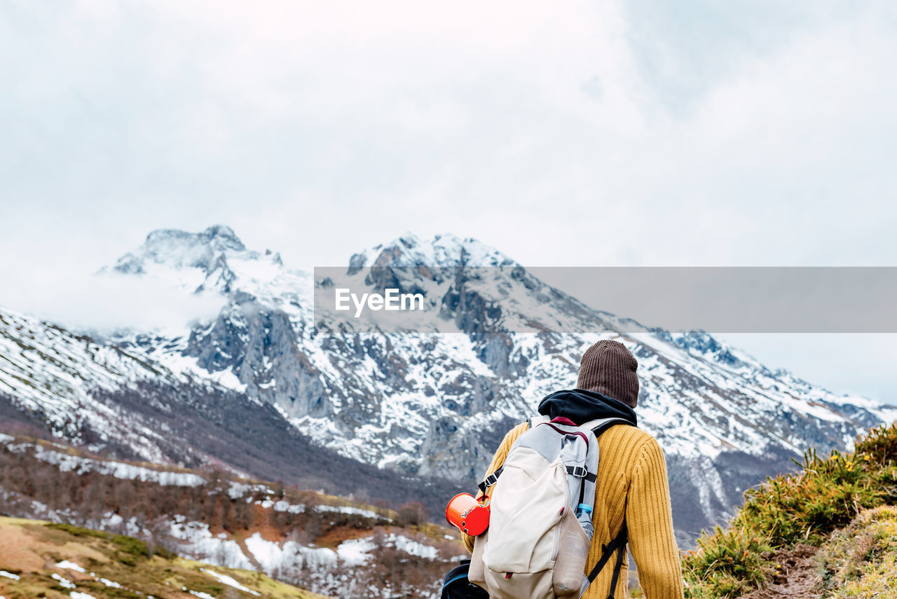 Back view of anonymous tourist with backpack standing on snowy lawn in valley of mountains in peaks of europe