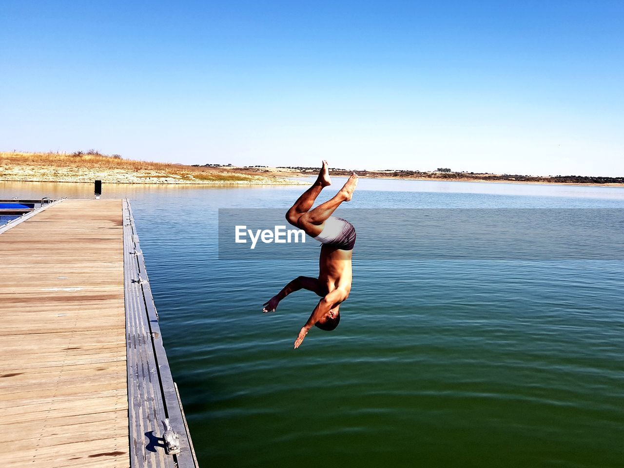 Full length of shirtless man jumping in lake against clear sky