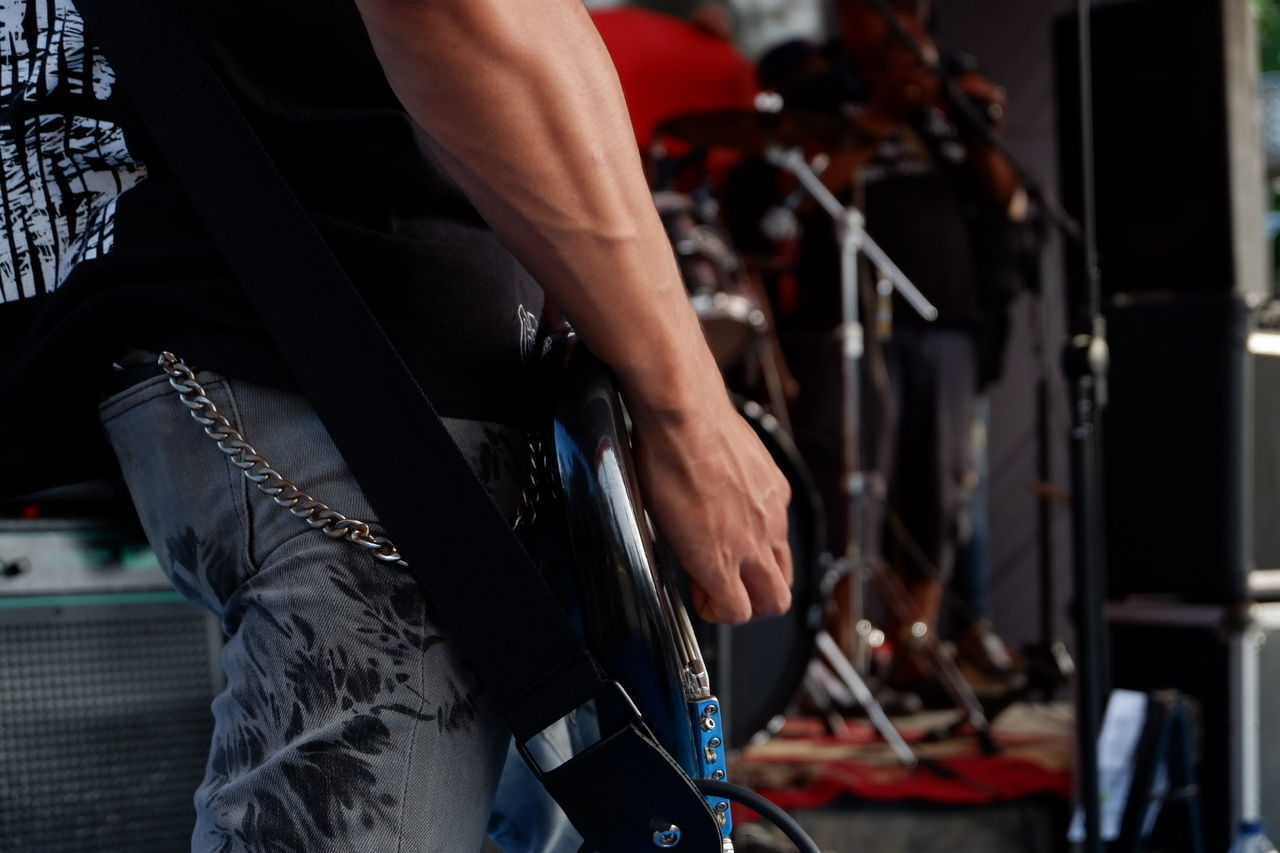 Midsection of musician playing electric guitar while standing on stage