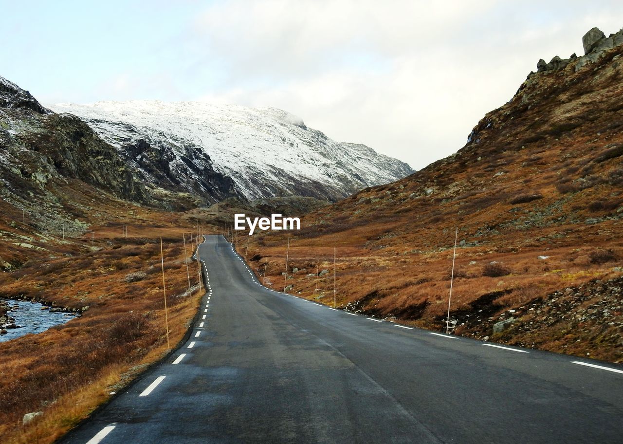 Empty road amidst snowcapped mountains against sky