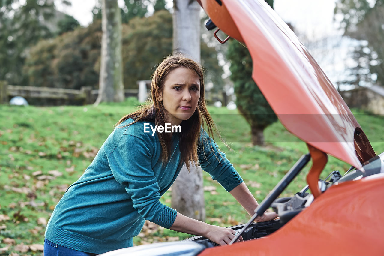 Sad or angry beautiful woman inspecting the engine for car 