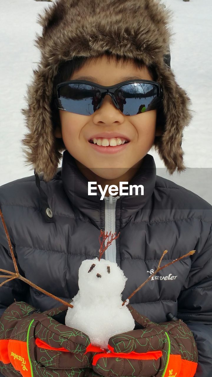 Portrait of smiling boy wearing warm clothing while holding small snowman