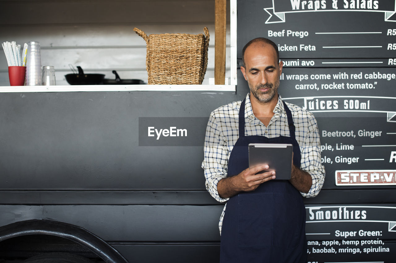 Male vendor using tablet computer while standing against food truck