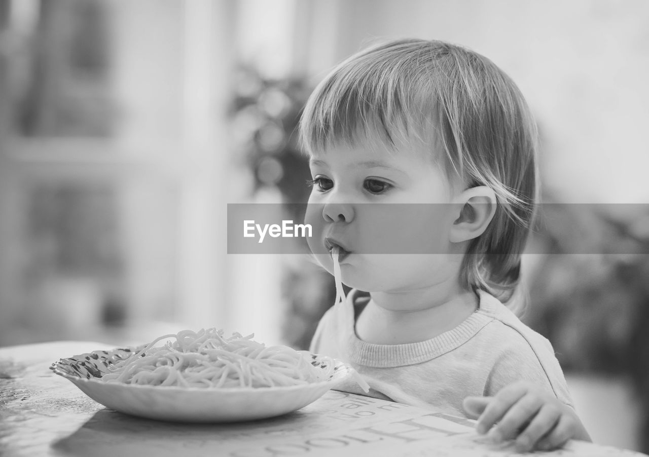 Charming baby girl eating spaghetti by hands