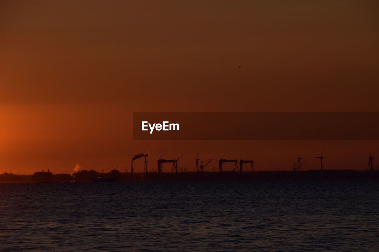 Silhouette cranes against sky during sunset