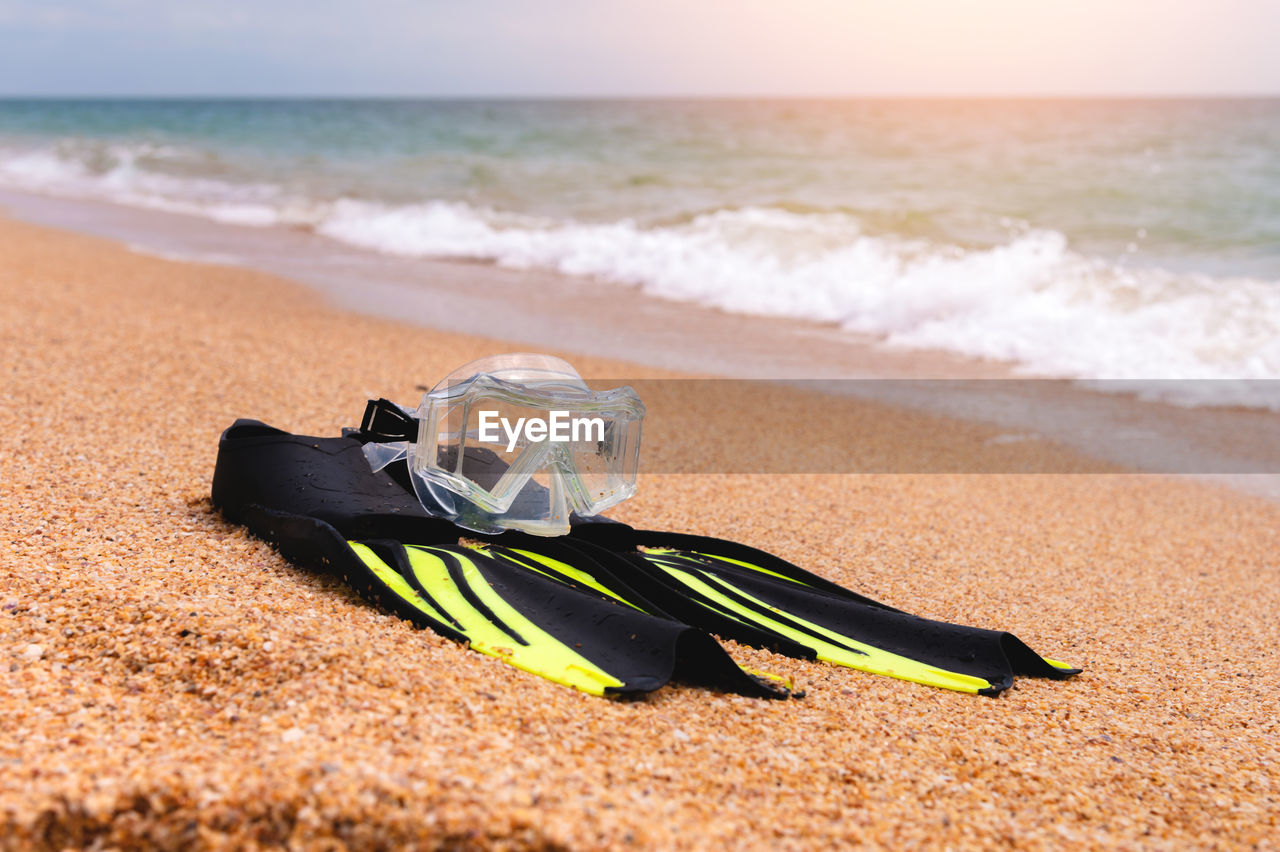 Shallow depth of field snorkeling mask with fins lies on a sandy beach overlooking the sea and sky