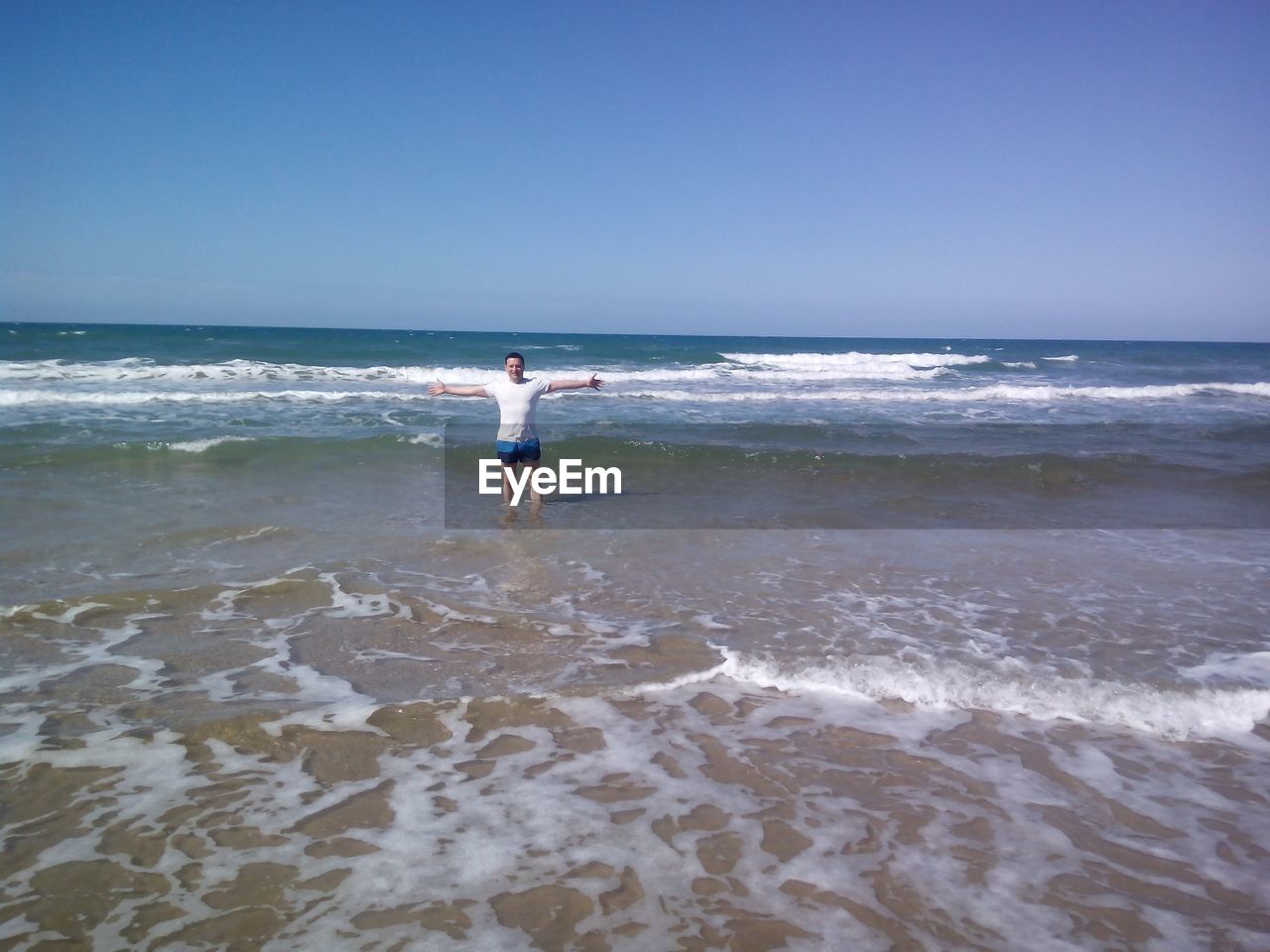 Man with arms outstretched standing in sea against clear sky