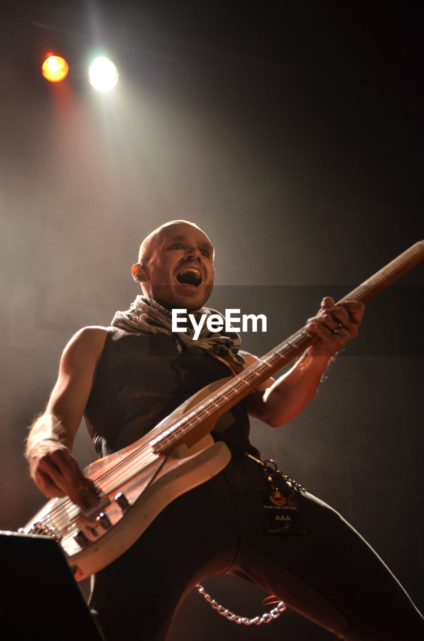 LOW ANGLE VIEW OF MAN PLAYING GUITAR AT MUSIC CONCERT