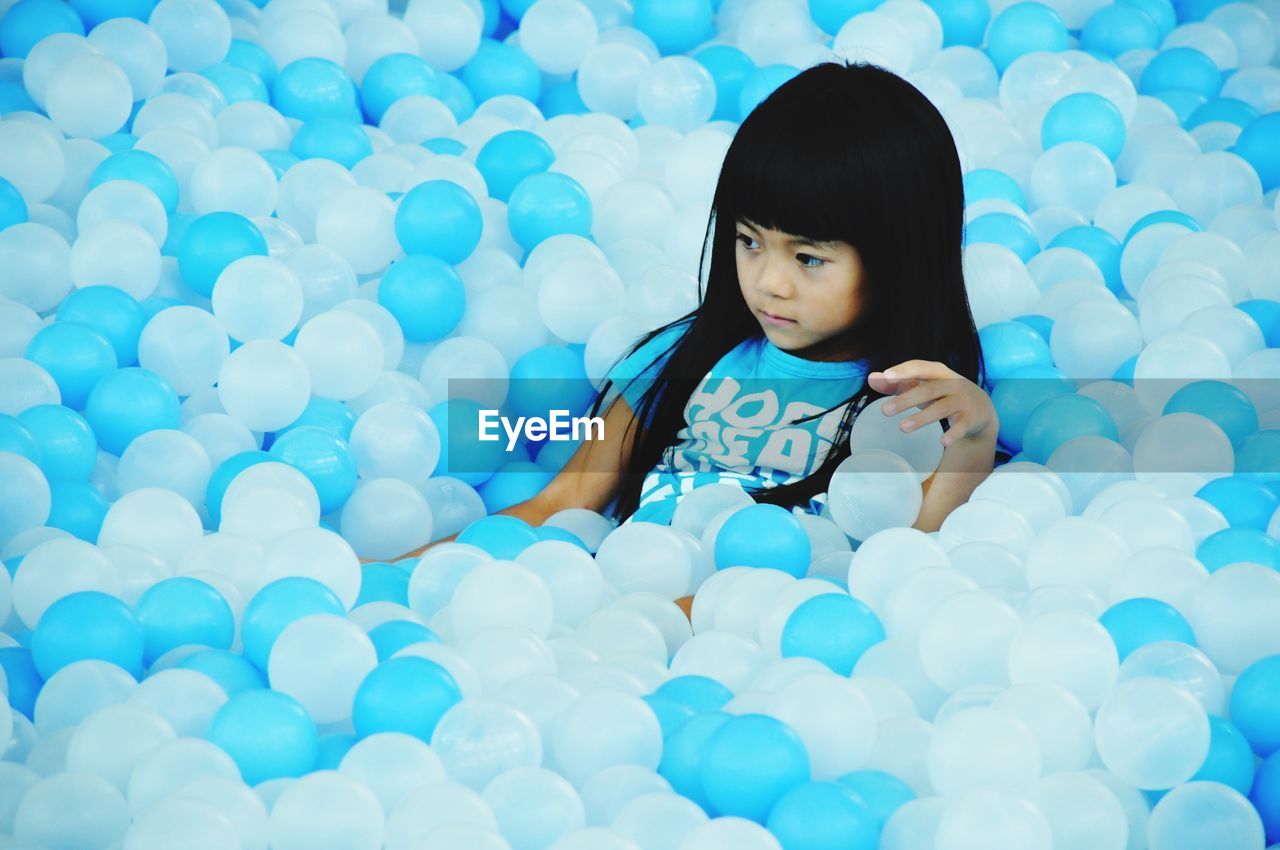 Cute girl looking away while sitting amidst blue and white helium balloons