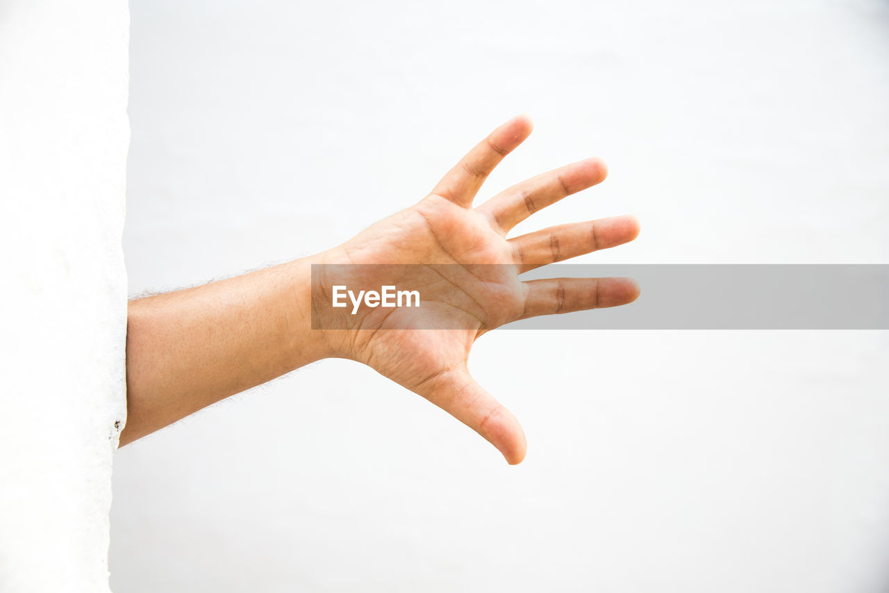 Cropped hand of man showing stop gesture against wall