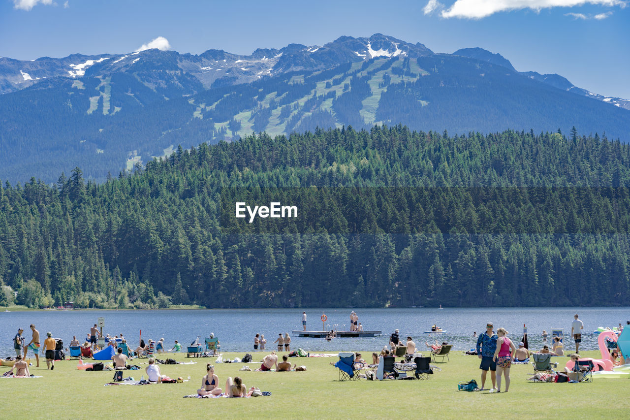 People on field by lake against mountains