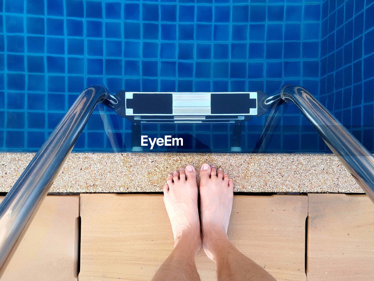 Low section of person standing by ladder in swimming pool