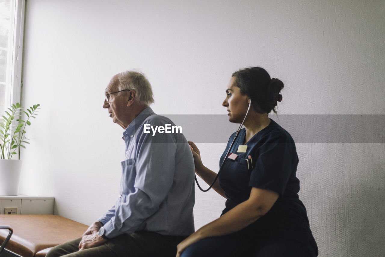 Mature female healthcare worker examining senior patient sitting in clinic