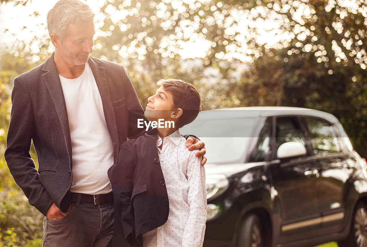 Smiling man looking at son against car on road