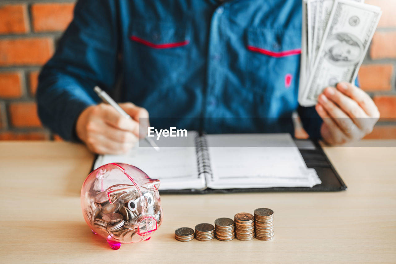 Midsection of man counting money in piggy bank