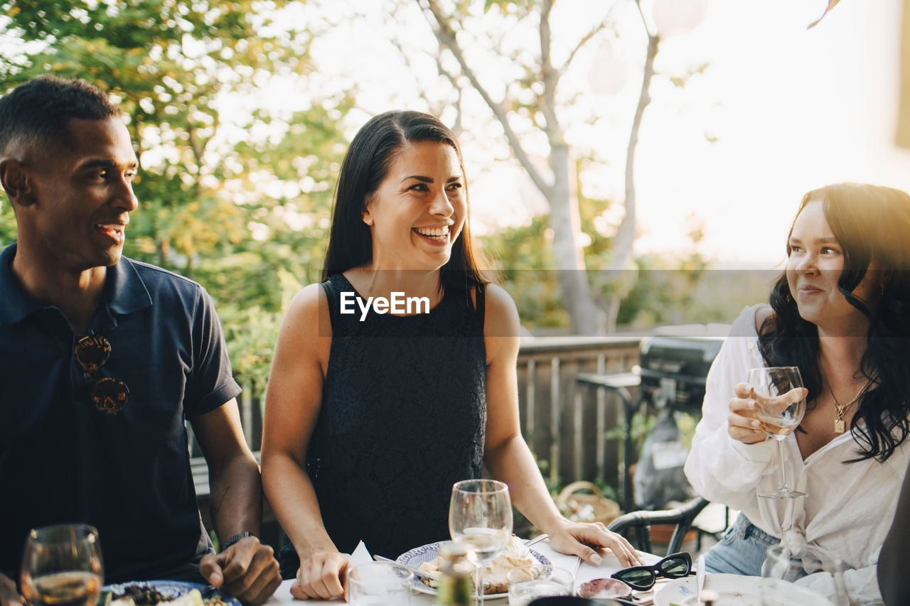 Smiling male and female friends enjoying food at dining table in dinner party