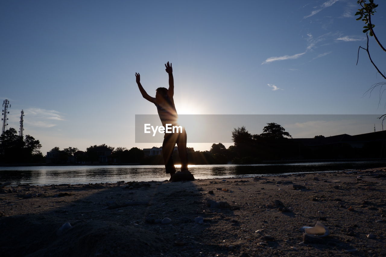 Rear view of woman jumping at beach against sky