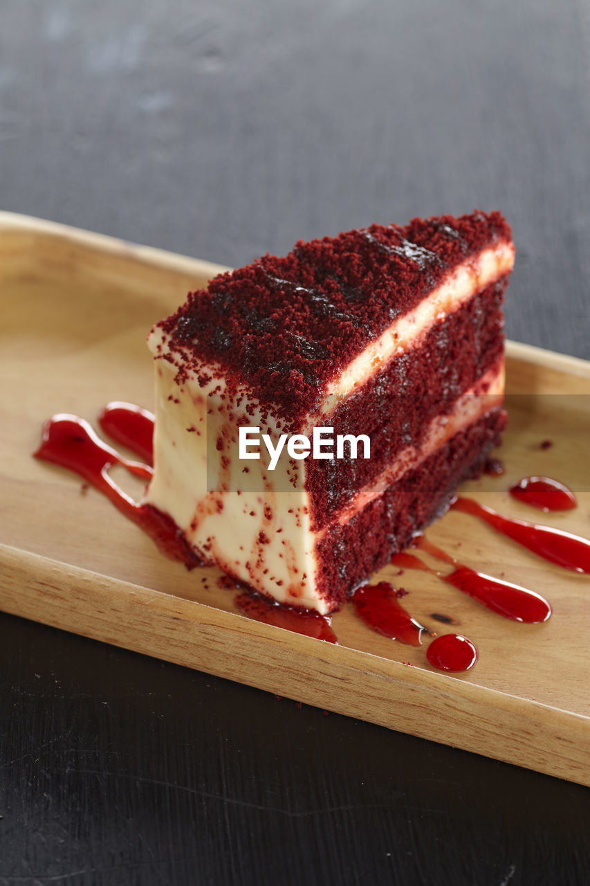 High angle view of red velvet cheesecake slice in wooden plate on table