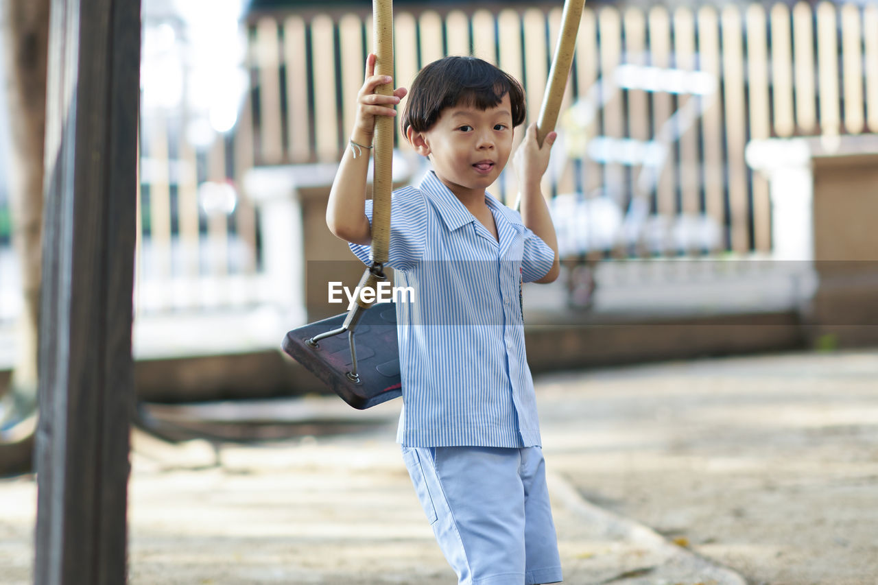 Cute boy holding swing while standing outdoors in playground 