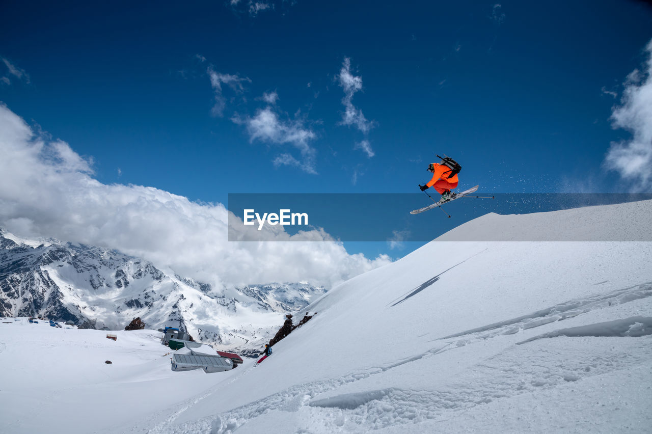 Professional athlete young male skier in an orange ski suit flies over the mountains after jumping