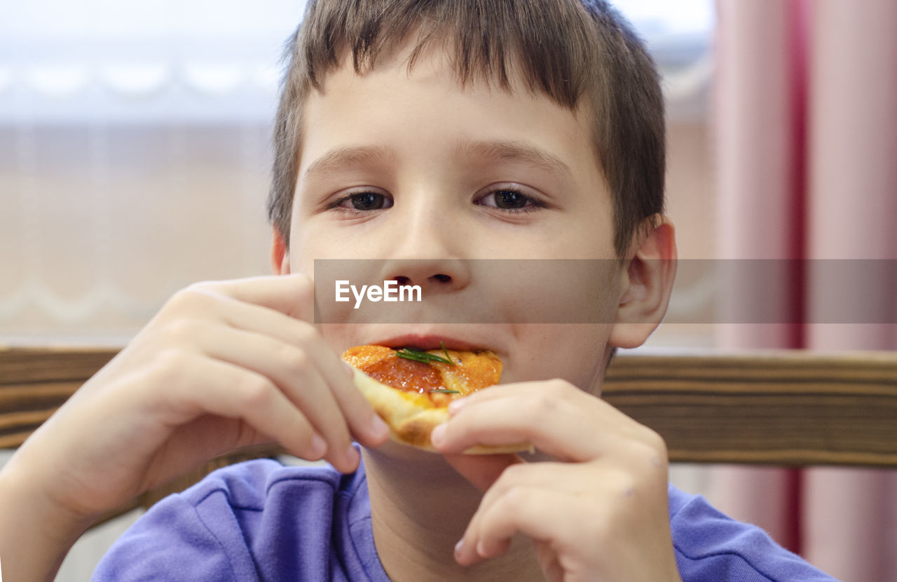 Boy eating pizza. child closed his eyes in pleasure and takes a bite of pizza piece holding it aloft