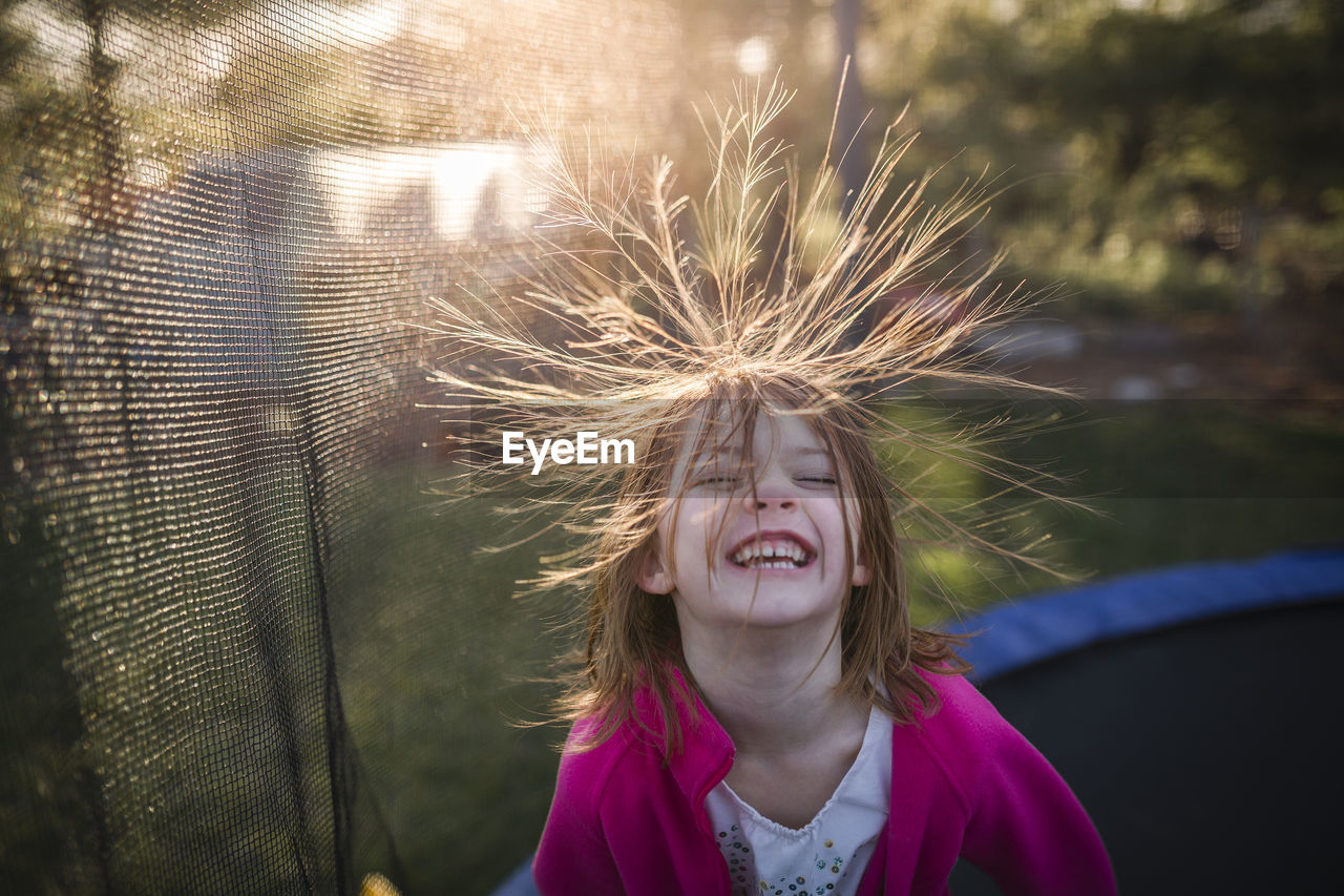 High angle view of cheerful girl jumping on trampoline in backyard