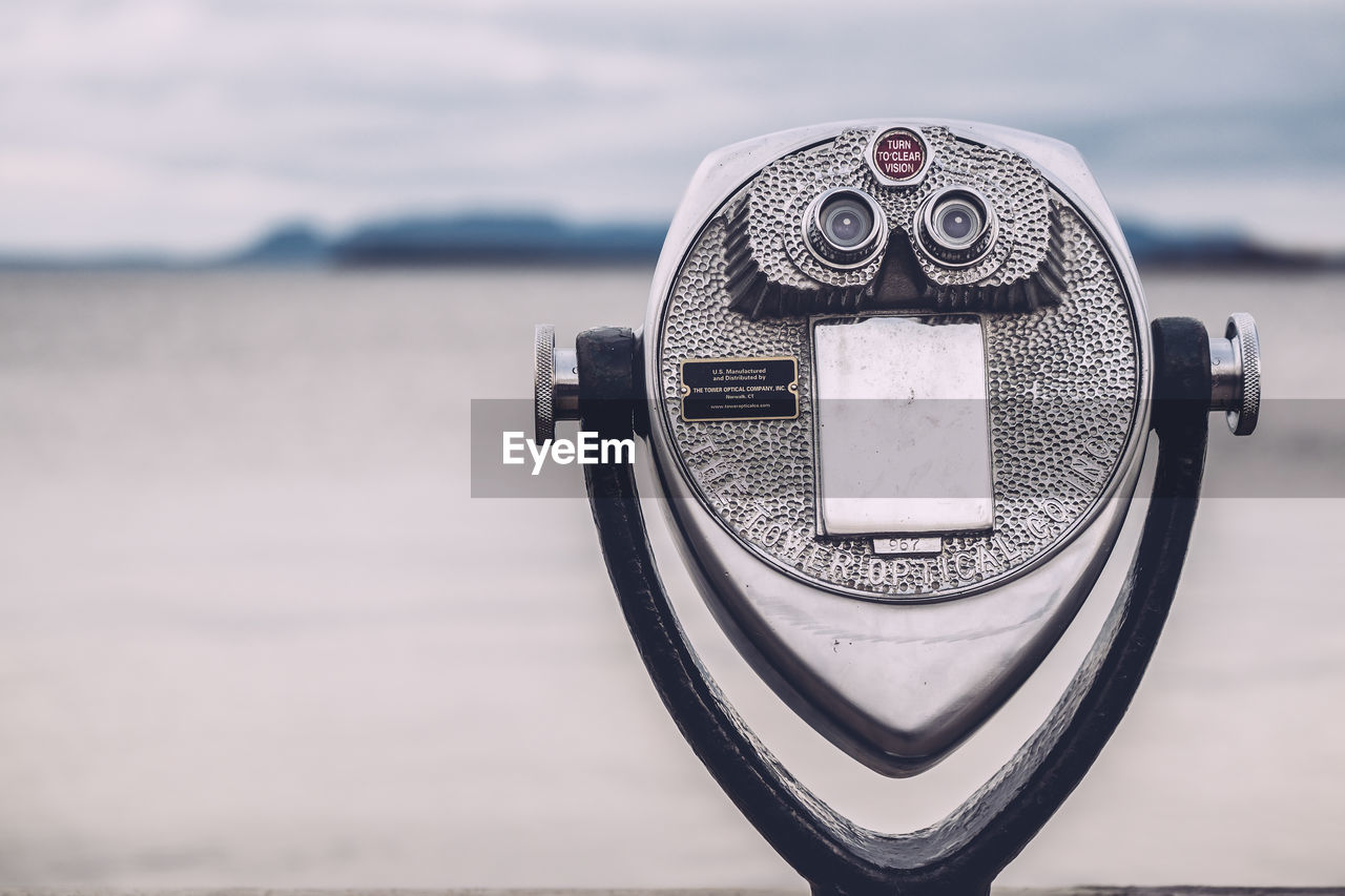 Close-up of coin-operated binoculars at beach against cloudy sky