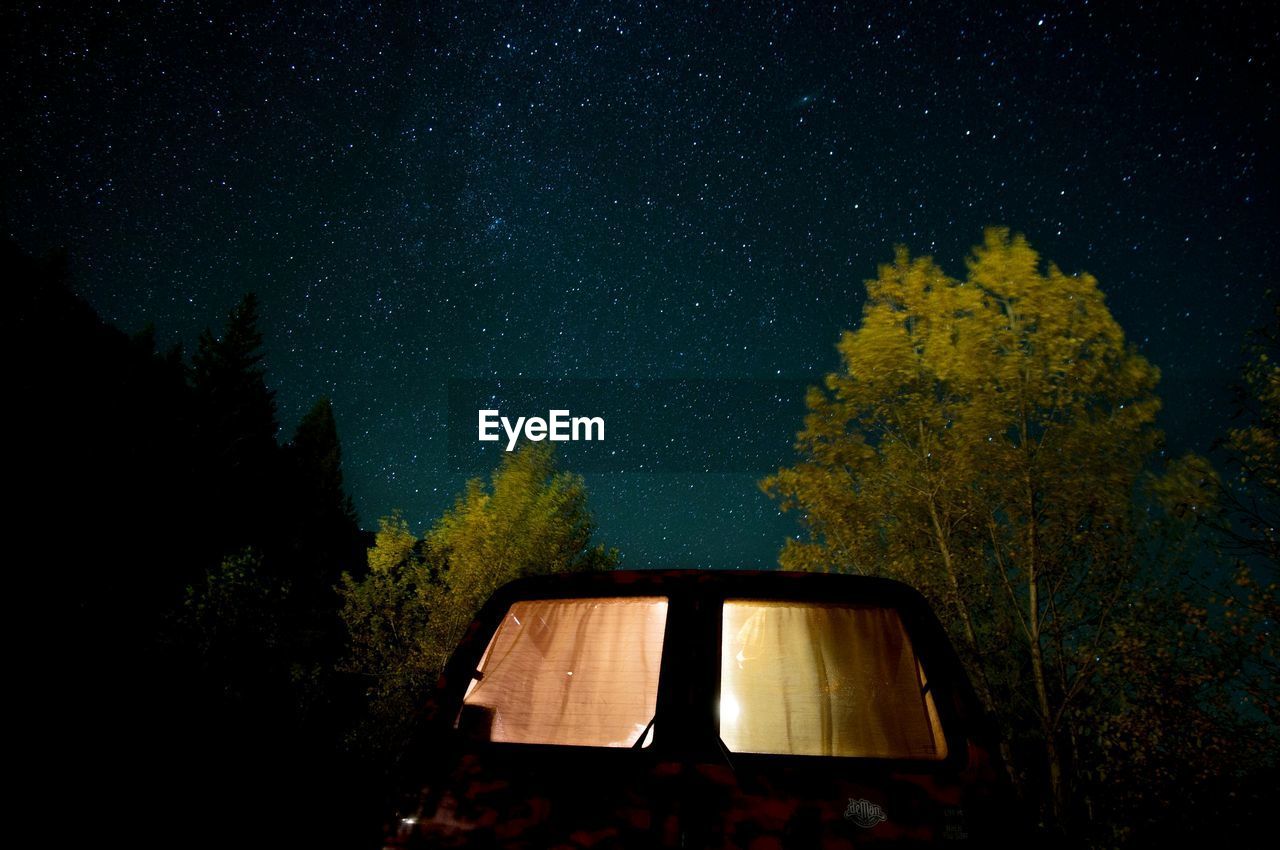 Illuminated motor home by trees against sky at night