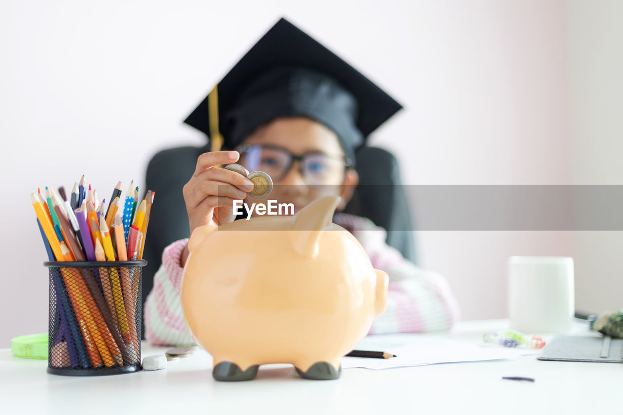 Girl inserting coins in piggy bank against white background