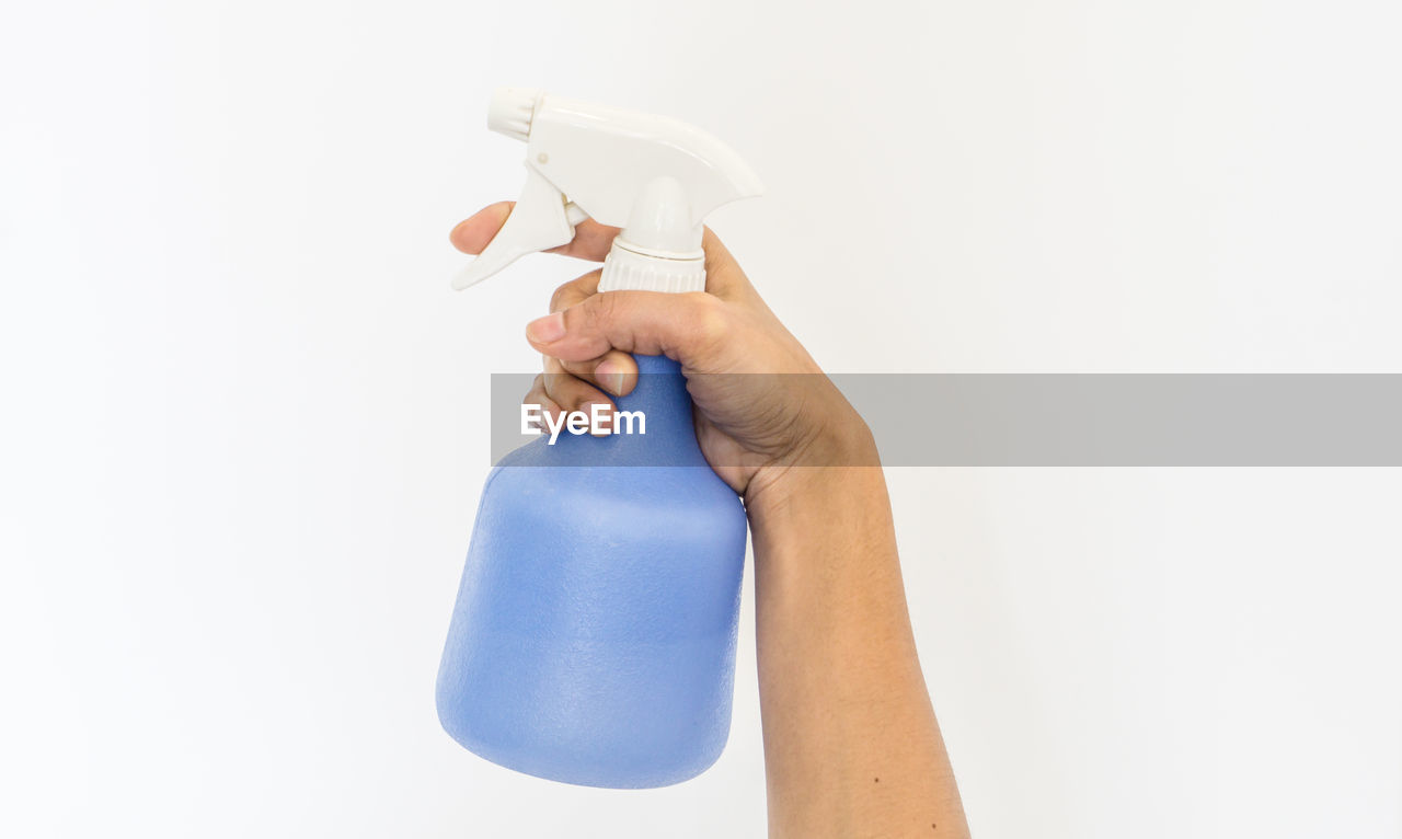 Close-up of person holding sprayer against white background