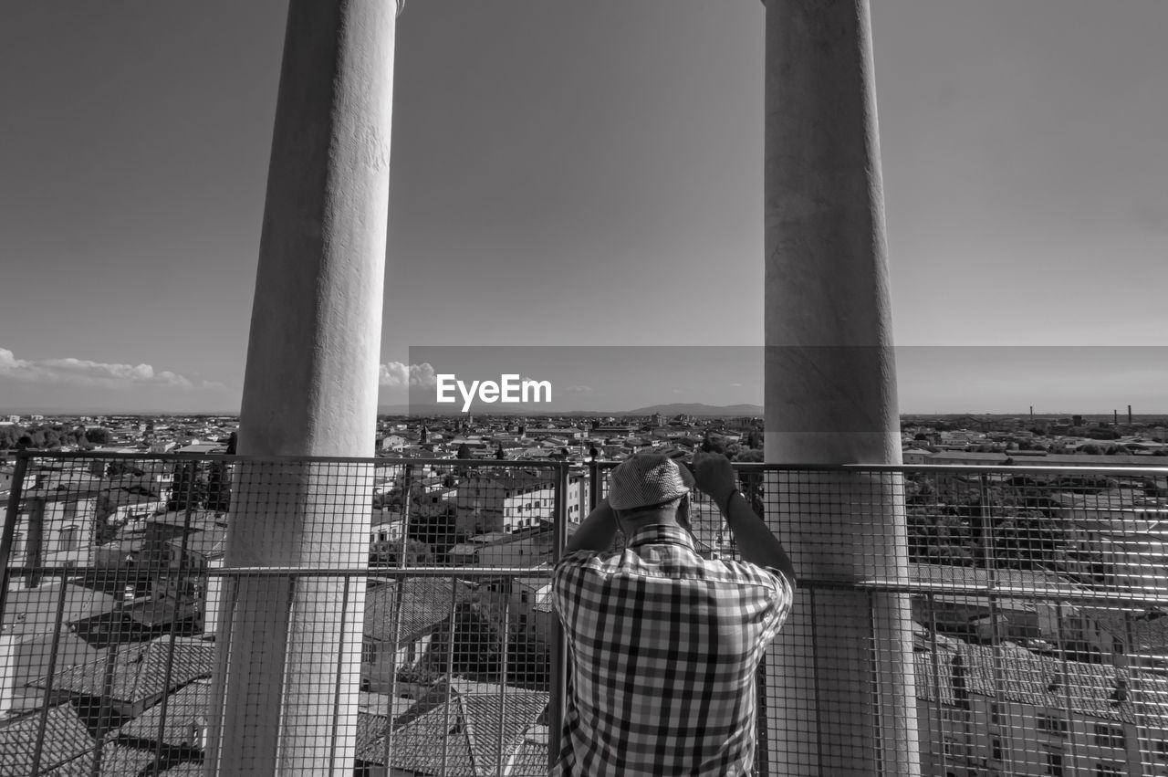 Rear view of man looking at buildings in city from balcony