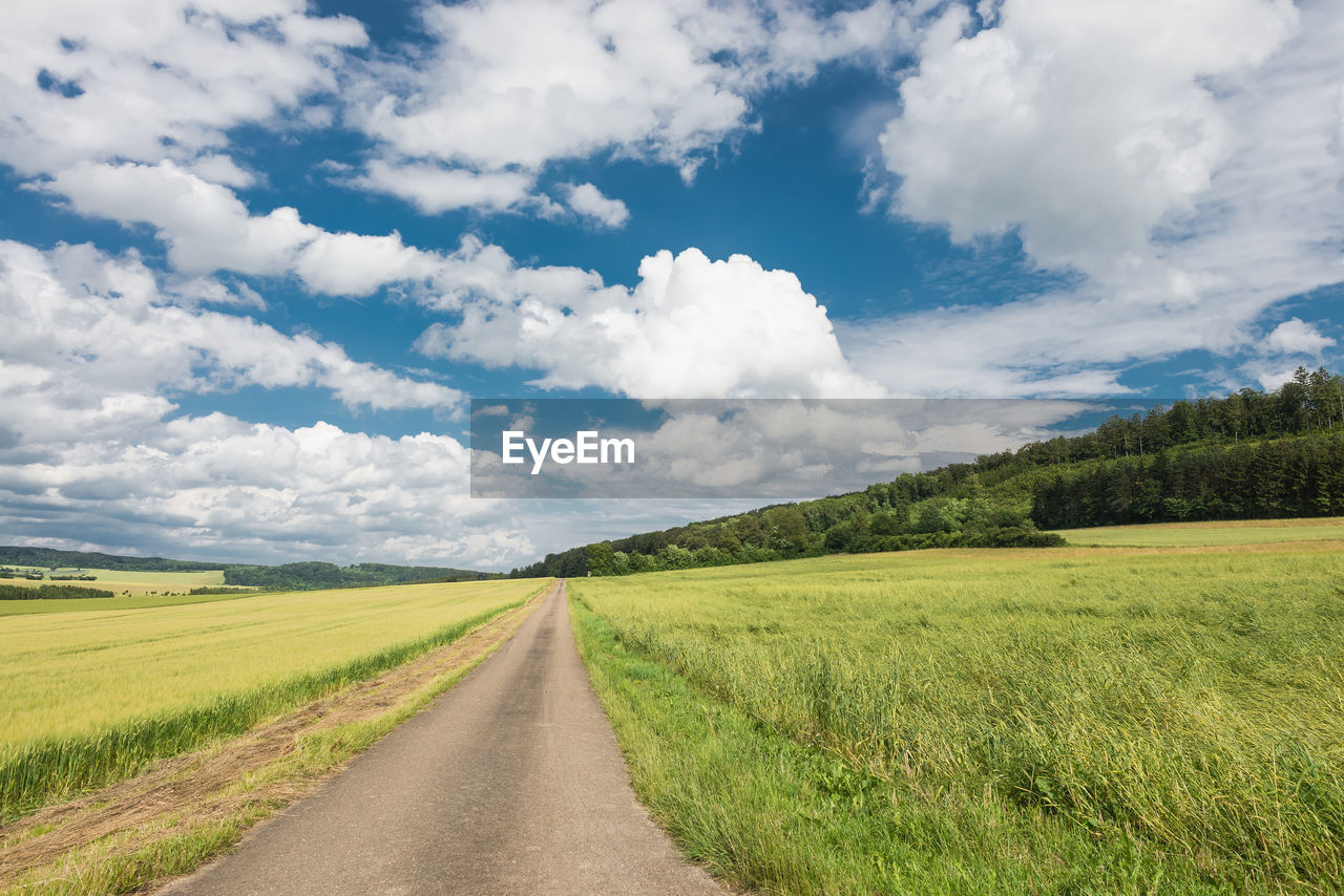 Street amidst grassy field against cloudy sky