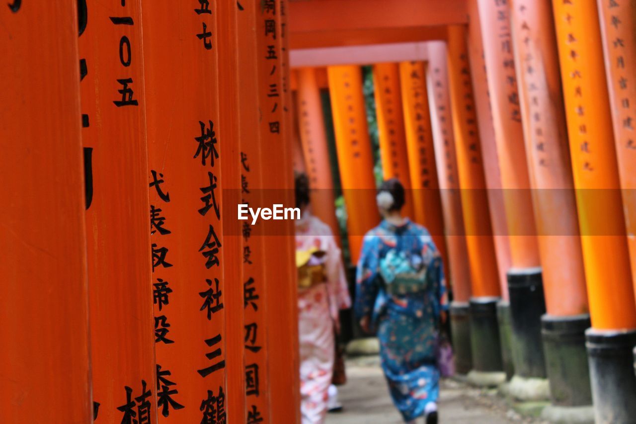 Rear view of women in traditional clothing walking between torii gates