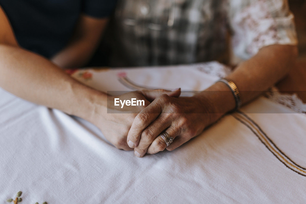 Female healthcare worker holding wrinkled hand of senior woman at home