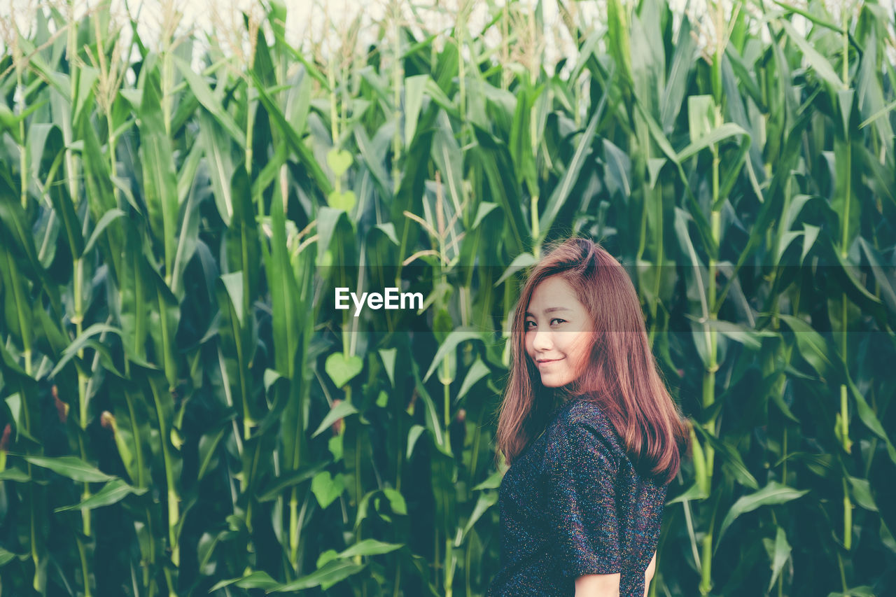 Portrait of smiling woman standing against crops in farm