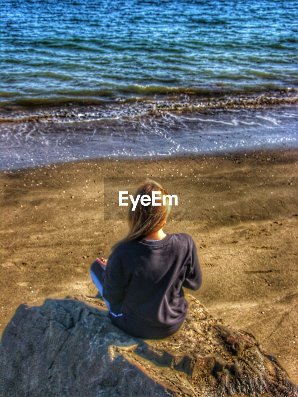 REAR VIEW OF WOMAN SITTING ON SAND AT BEACH