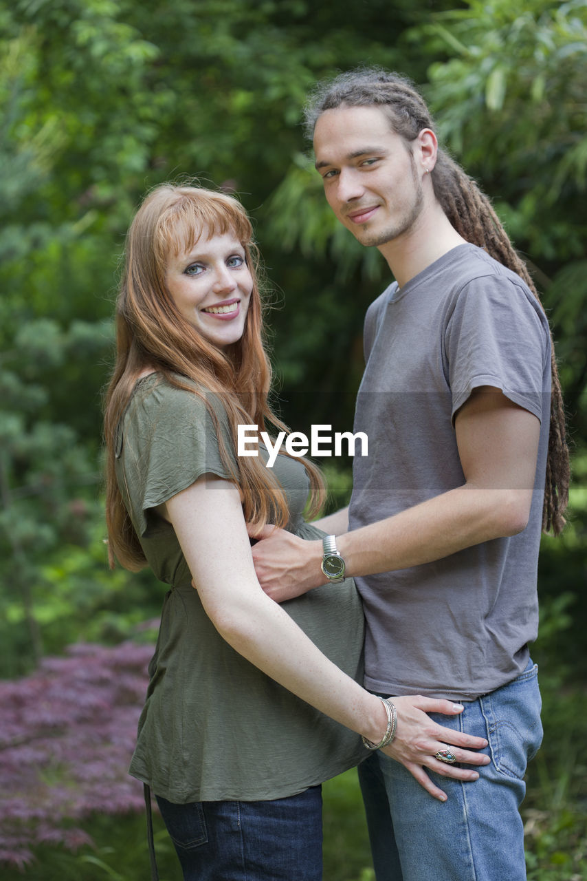 Portrait of man standing with pregnant woman against trees