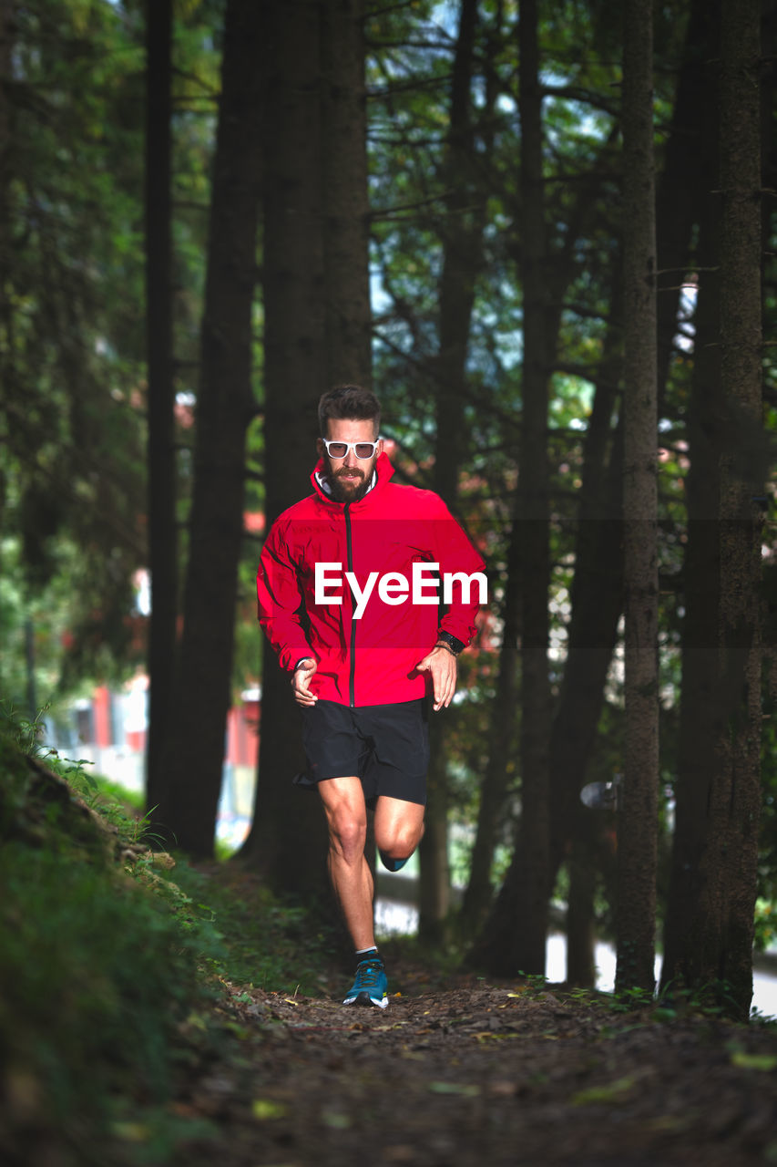 FULL LENGTH OF MAN RUNNING ON TREE IN FOREST