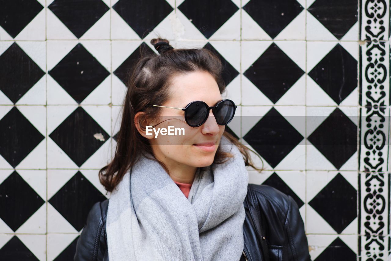 Smiling beautiful woman wearing sunglasses against patterned tiled wall