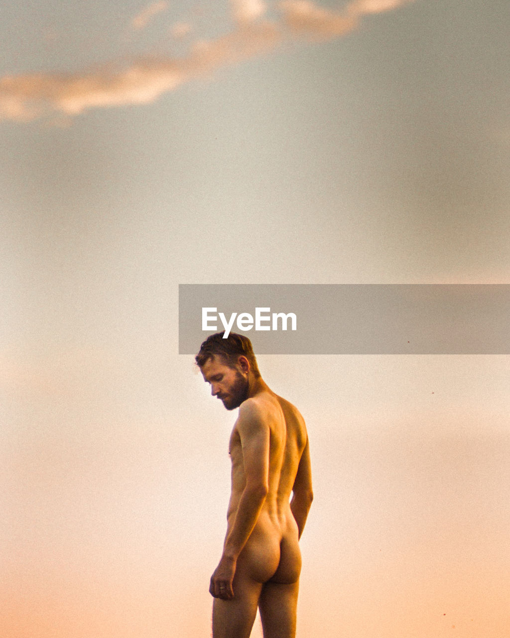 Rear view of naked man standing against sky during sunset