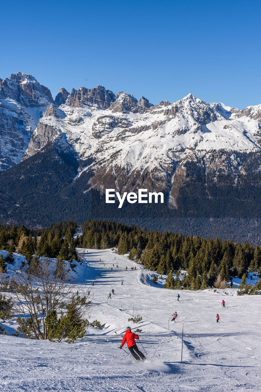 Person skiing on snowcapped mountains against clear blue sky