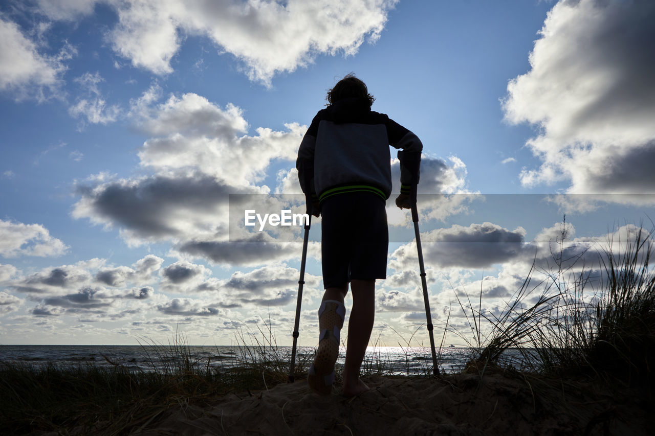 REAR VIEW OF MAN STANDING AT BEACH