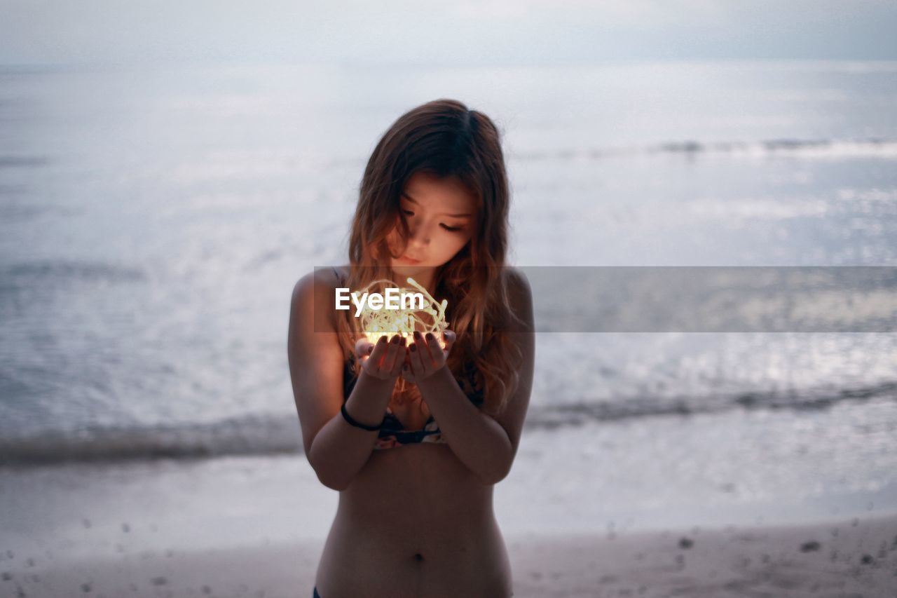 Beautiful young woman holding lights at beach